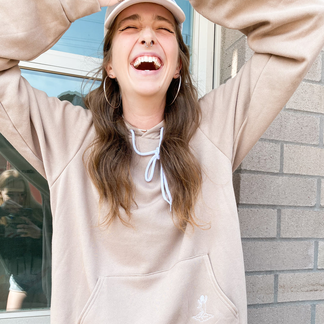 Smiling model wearing tan sweatshirt and hoop earnings 