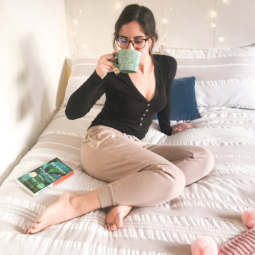 Model wearing comfy tan sweatpants in bed reading a book