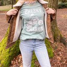 Load image into Gallery viewer, girl wearing light blue t shirt in the forest. The t shirt features a cherub riding a motorcycle and says &#39;The Cheeky Cherub&#39;
